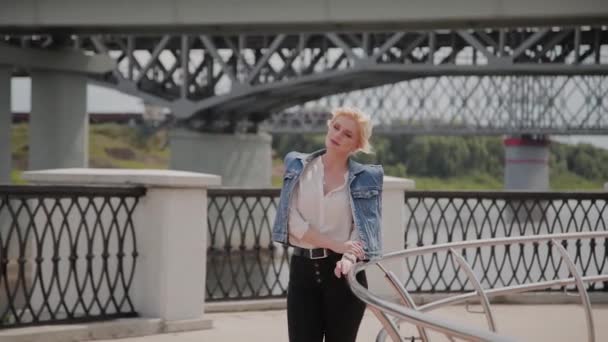 Mooie jonge vrouw loopt langs de dijk bij de rivier en geniet van wat er gebeurt. — Stockvideo