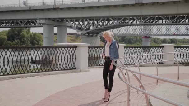 Beautiful young woman walks along the embankment by the river and enjoys what is happening. — Stock Video