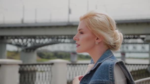 Mooie jonge vrouw loopt langs de dijk bij de rivier en geniet van wat er gebeurt. — Stockvideo