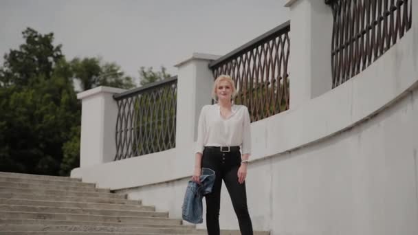 Beautiful young woman walks along the embankment by the river and enjoys what is happening. — Stock Video