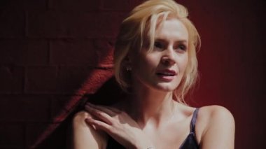 Güzel ve romantik kadın sert güneşin altında kırmızı duvarın yanında duruyor.