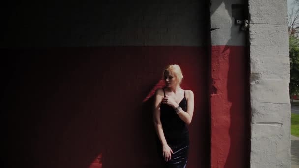 Belle et romantique femme se tient près du mur rouge sous le soleil rude . — Video