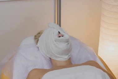Krem emmek için kapalı bir yüz ile bir güzellik salonunda bir kanepede yatan kadın.