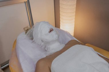 Krem emmek için kapalı bir yüz ile bir güzellik salonunda bir kanepede yatan kadın.