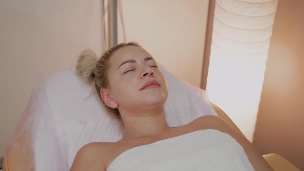 Hermosa mujer joven en albornoz acostada y esperando procedimiento de cuidado facial en el salón de spa de lujo — Vídeo de stock