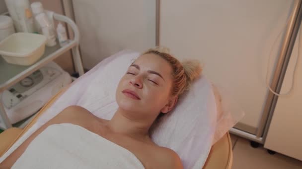 Beautiful young woman in bathrobe lying and waiting facial care procedure at luxury spa salon — Stock Video