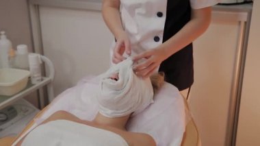 Profesyonel bir güzellik uzmanı bir kadının suratından bir havluyu çıkarır ve siler..