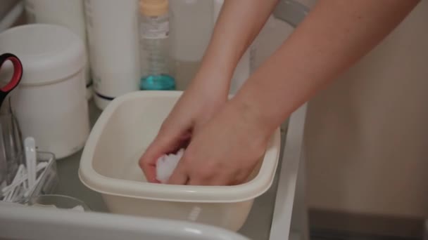 El proceso de preparación de toallitas húmedas para limpiar la piel. Las manos de un esteticista de cerca. Solución acuosa en una taza blanca. Procedimiento cosmético en el salón de belleza — Vídeos de Stock