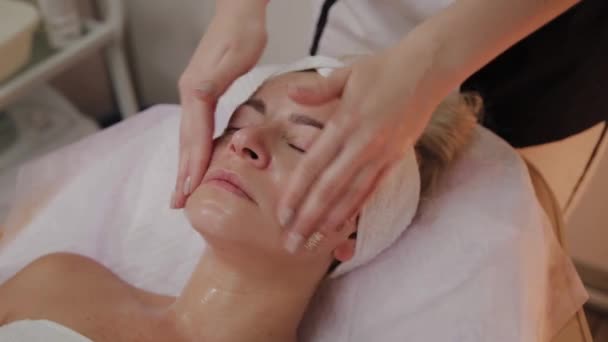 Spa mulher facial Massagem. Massagem facial no salão de beleza spa. Feminino desfrutando de relaxante massagem facial no centro de spa cosmetologia. Cuidados com o corpo, cuidados com a pele, bem-estar, tratamento de beleza . — Vídeo de Stock