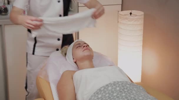 Mujer en el procedimiento en la esteticista con una toalla en la cara . — Vídeo de stock