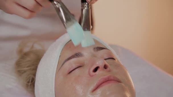 Επαγγελματική αισθητικός εφαρμογή μάσκα με βούρτσες στο πρόσωπο της γυναίκας. — Αρχείο Βίντεο