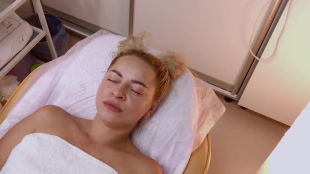 Красивая молодая женщина в халате лежит и ждет процедуры по уходу за лицом в роскошном спа-салоне — стоковое видео