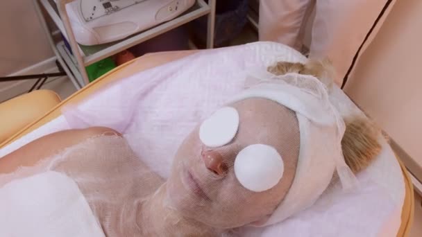 Hermosa mujer joven en albornoz acostada y esperando procedimiento de cuidado facial en el salón de spa de lujo — Vídeos de Stock