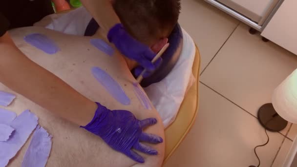 Professionele schoonheidsspecialiste maakt waxen aan een man in een schoonheidssalon. — Stockvideo