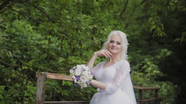 Bella sposa bionda su un ponte vicino alla ringhiera nella foresta . — Video Stock