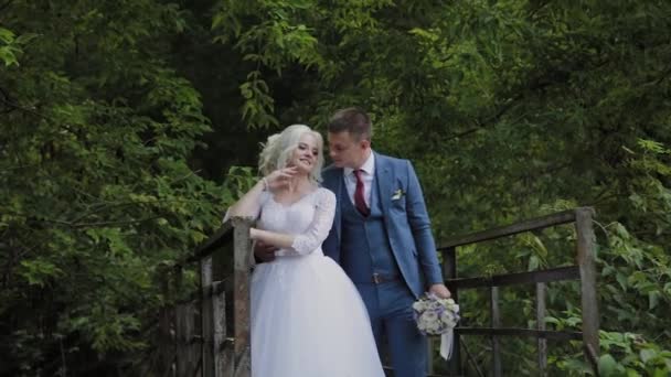 Krásná nevěsta a ženich na starém železném mostě v lese. Ženich pohladil svou milovanou. — Stock video