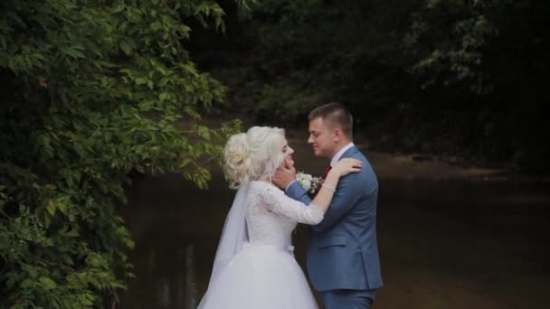 Krásný ženich a blonďatá nevěsta u potoka v lese. — Stock video