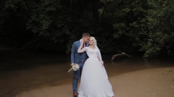 Beau marié et mariée blonde au bord du ruisseau dans la forêt . — Video