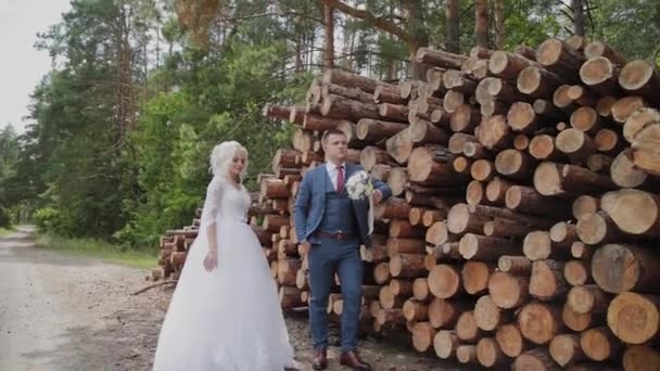 Mooie bruidegom en blonde bruid door de logs in het bos knuffel en kus. — Stockvideo