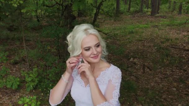Красивая блондинка невеста в лесу гладит себя, выпрямляет волосы . — стоковое видео