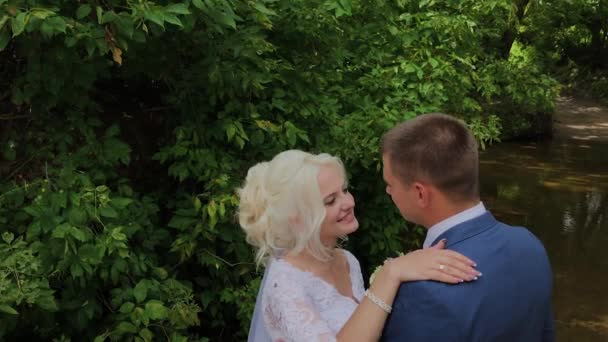 Mooie bruidegom en blonde bruid door de kreek in het bos. — Stockvideo