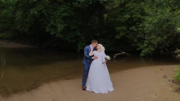 Krásný ženich a blonďatá nevěsta u potoka v lese. — Stock video