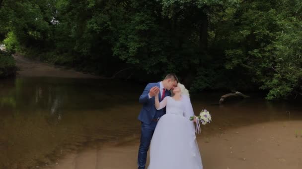 Beautiful groom and blonde bride by the creek in the forest. — Stock Video