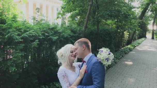 Joyeux jeunes mariés marchent dans le parc en se tenant la main, embrasser baiser . — Video