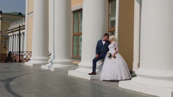 Happy newlyweds stand at the columns in the park. — Stock Video