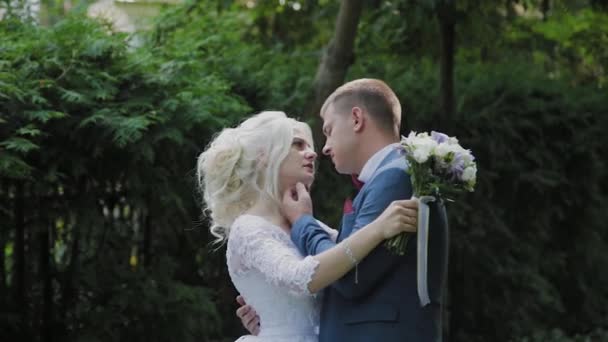 Gli sposi felici camminano nel parco tenendosi per mano, abbracciandosi bacio . — Video Stock