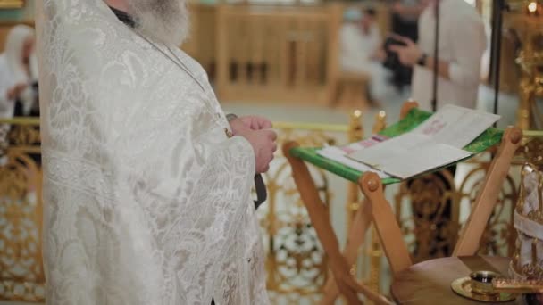 Een oude priester staat aan het altaar en leest een gebed. — Stockvideo