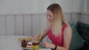 Güzel genç kız bir kafede bir masada oturur ve bir tabak tatlı taze tatlılar yiyor.