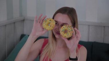 Güzel kız bir kafede bir masada elinde donut ile poz.