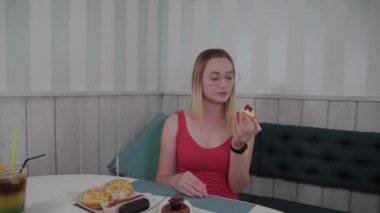 Güzel genç kız bir kafede bir masada oturur ve bir tabak tatlı taze tatlılar yiyor.