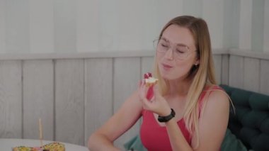 Güzel genç kız bir kafede bir masada oturur ve bir tabak tatlı taze tatlılar yiyor.