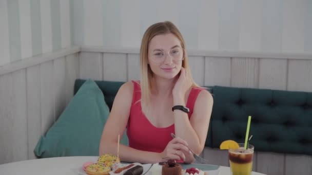 Hermosa joven sentada en una mesa en un café con un plato de postres . — Vídeo de stock