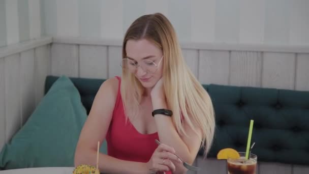 Hermosa joven sentada en una mesa en un café con un plato de postres . — Vídeo de stock