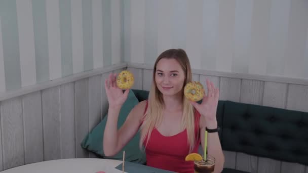 Mooi meisje poseren met donuts in handen aan een tafel in een café. — Stockvideo