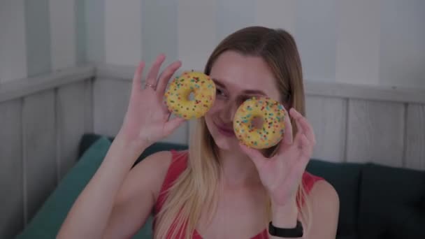 Schönes Mädchen posiert mit Donuts in den Händen an einem Tisch in einem Café. — Stockvideo