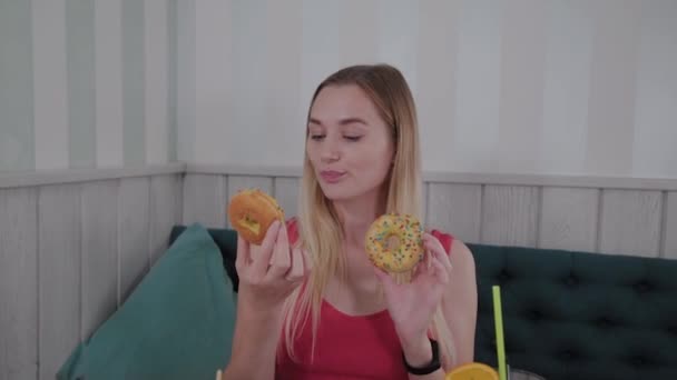 Menina bonita posando com donuts nas mãos em uma mesa em um café . — Vídeo de Stock