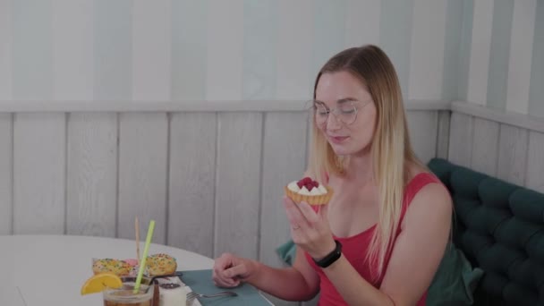 Vacker ung flicka sitter vid ett bord på ett kafé och äter söta färska desserter från en tallrik. — Stockvideo