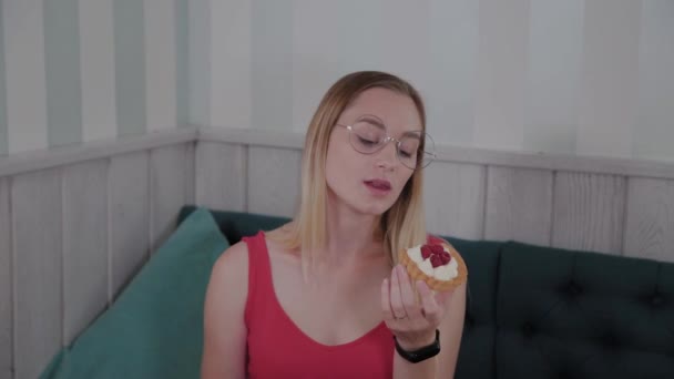 Hermosa joven se sienta en una mesa en un café y come dulces postres frescos de un plato . — Vídeos de Stock