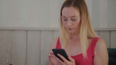 Güzel bir genç kız bir masada bir restoranda bir cep telefonu kullanır, onun etrafında tatlılar ile bir tabak.