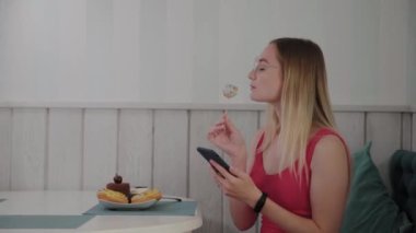 Güzel bir genç kız bir masada bir restoranda bir cep telefonu kullanır, onun etrafında tatlılar ile bir tabak.