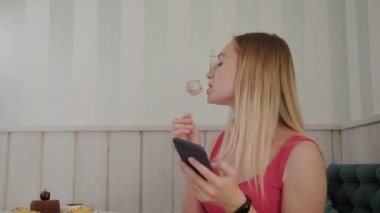Güzel bir genç kız bir masada bir restoranda bir cep telefonu kullanır, onun etrafında tatlılar ile bir tabak.