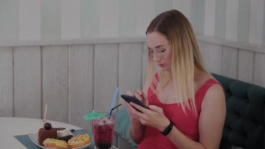 Güzel bir genç kız bir masada bir restoranda bir cep telefonu kullanır, onun etrafında tatlılar ile bir tabak.