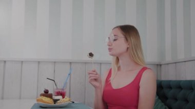 Güzel genç kız bir kafede bir masada oturur ve bir tabak tatlı taze tatlılar yiyor.