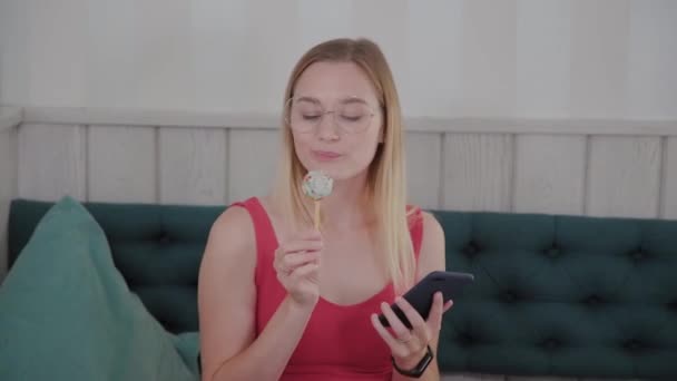 Uma menina bonita usa um telefone celular em um restaurante em uma mesa, em torno dela é um prato com sobremesas . — Vídeo de Stock