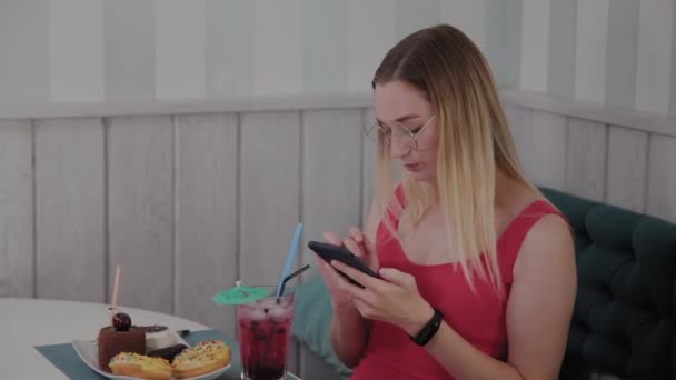 아름다운 어린 소녀는 테이블에서 레스토랑에서 휴대 전화를 사용, 그녀의 주위에 디저트와 접시입니다. — 비디오