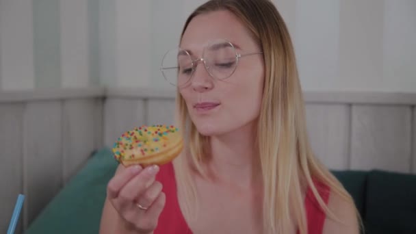 Hermosa joven se sienta en una mesa en un café y come dulces postres frescos de un plato . — Vídeos de Stock